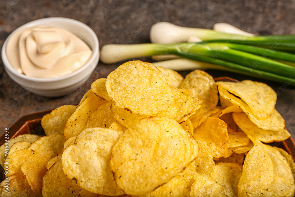 Bowl of tasty sour cream with green onion and potato chips on dark background