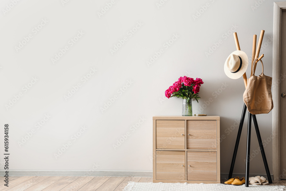 Vase of red peonies with coat rack and dresser near light wall