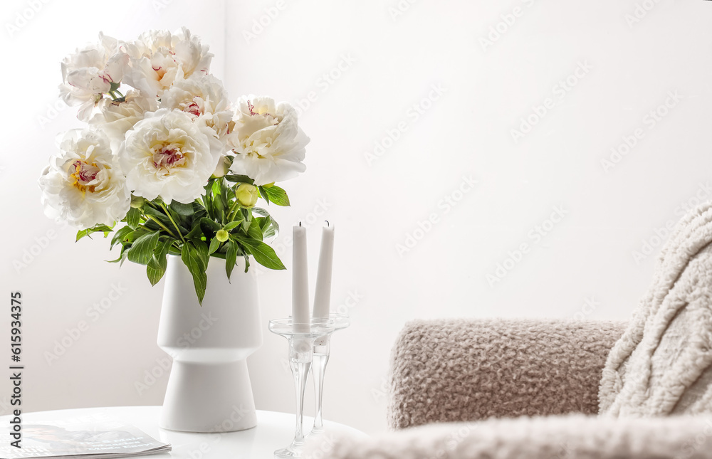 Vase of white peonies with candles and magazine on coffee table near wall