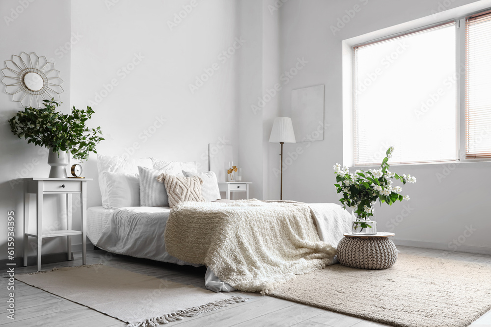 Interior of light bedroom decorated with blooming jasmine flowers in vase