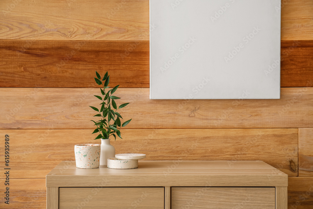 Beautiful branch, candles on table and blank frame hanging on wooden wall in room