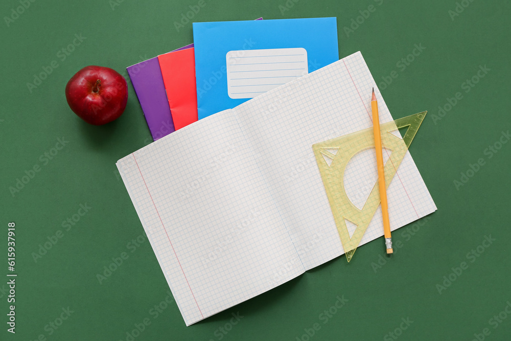 Notebooks with fresh red apple, ruler and pencil on green background