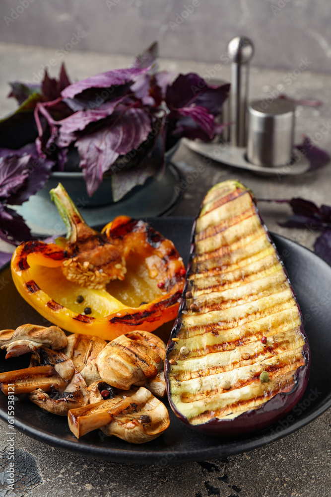 Plate with grilled vegetables and basil on grey background