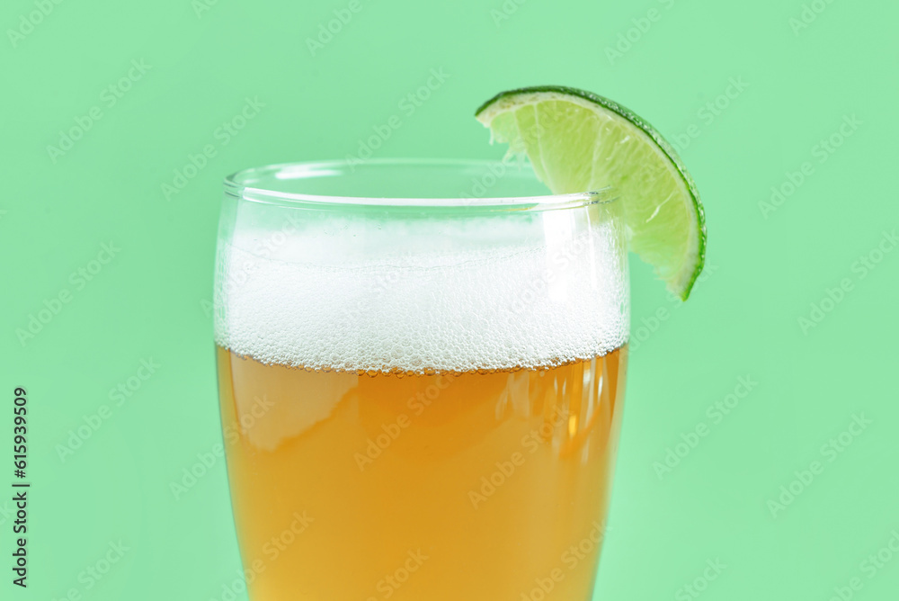 Glass of cold beer with lime on green background