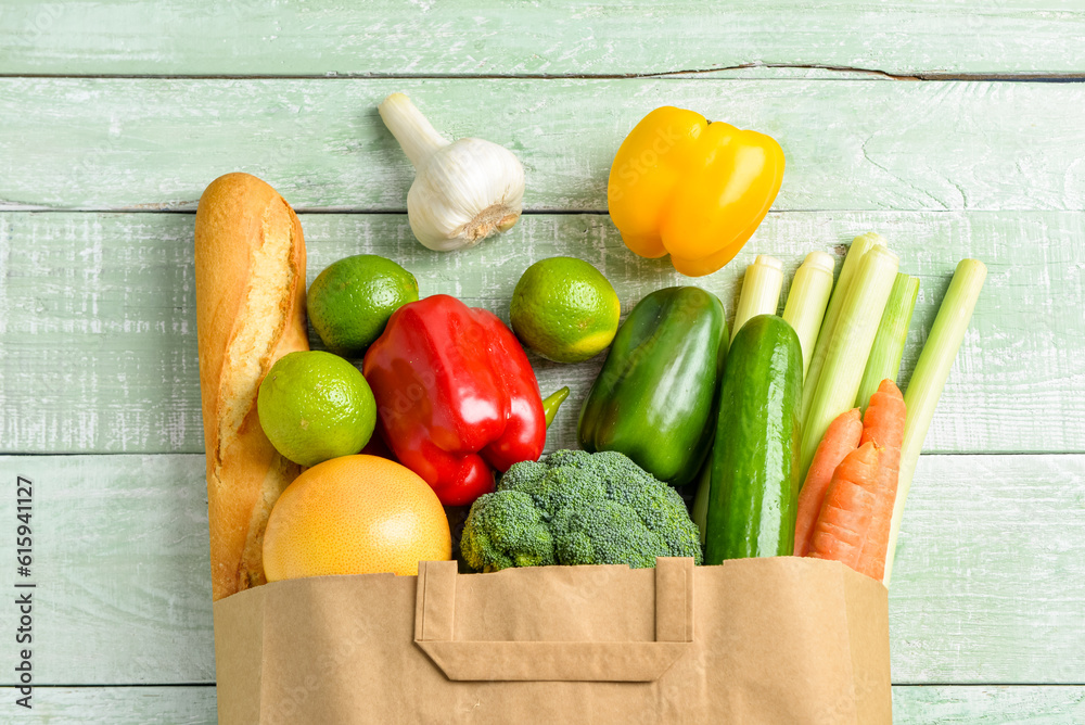 Paper bag with different products on green wooden background