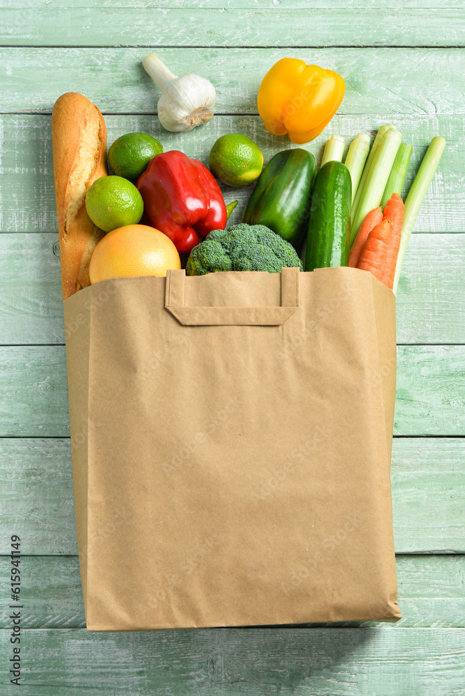 Paper bag with different products on green wooden background