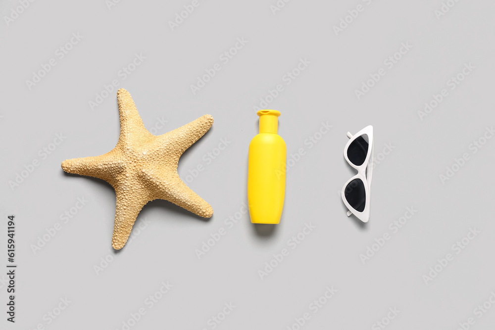 Sunglasses with starfish and bottle of sunscreen cream on grey background