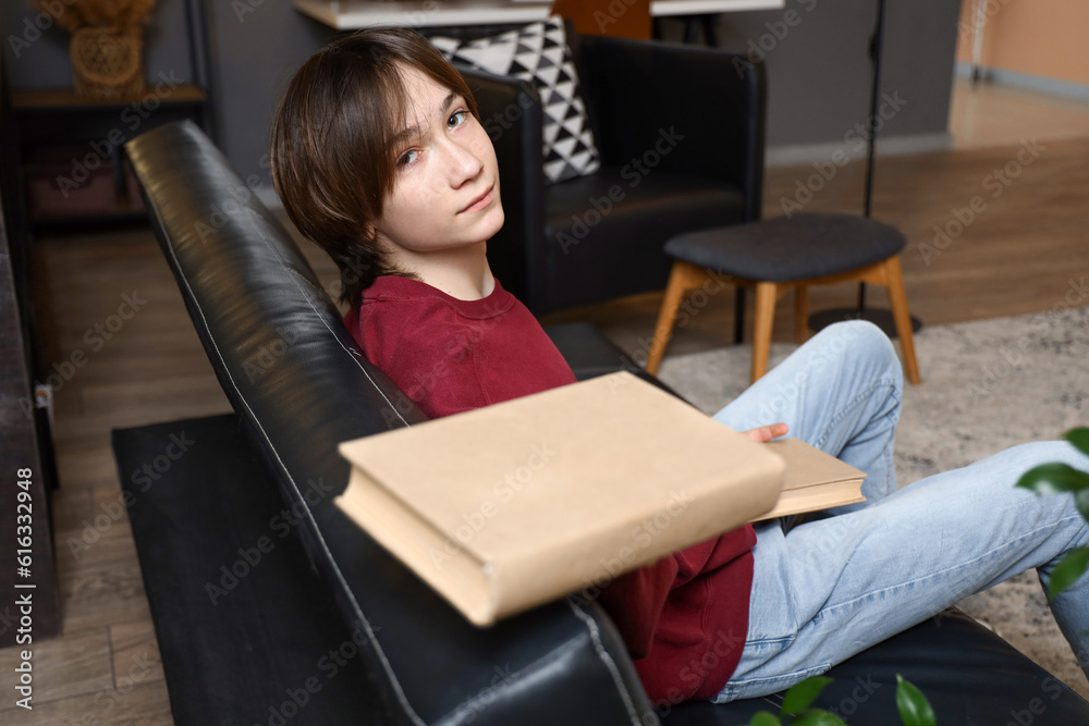 Teenage boy with books sitting on sofa at home late in evening