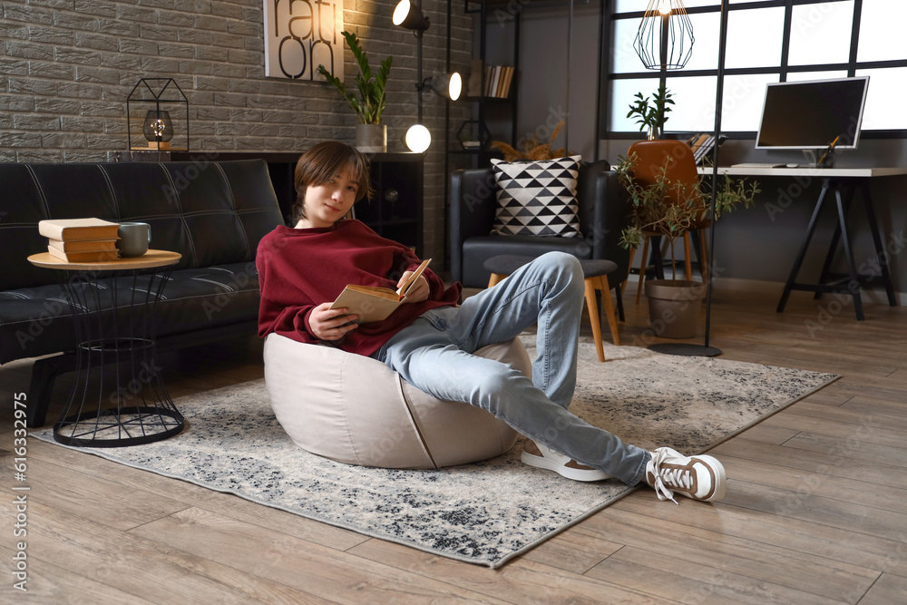 Teenage boy reading book at home late in evening