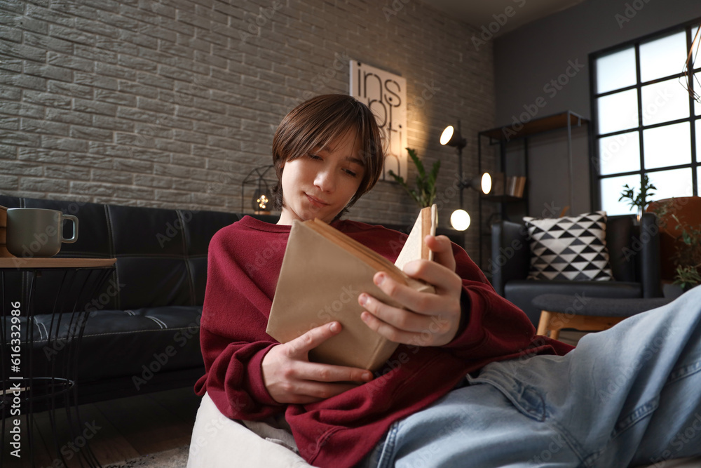 Teenage boy reading book at home late in evening