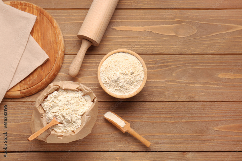 Composition with bowl of wheat flour, bag and rolling pin on wooden table