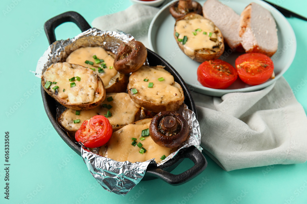 Baking dish with tasty baked potato, mushrooms and tomatoes on color background