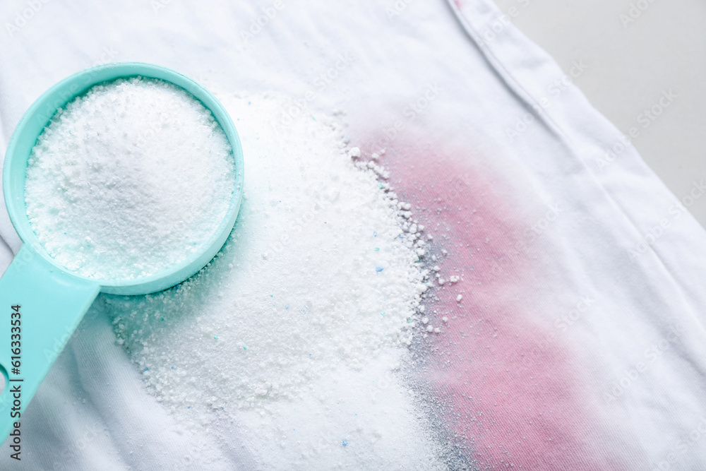 Laundry detergent with stained clothes on light background, closeup