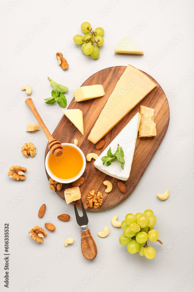 Wooden board with different types of tasty cheese, grapes and honey on grey background