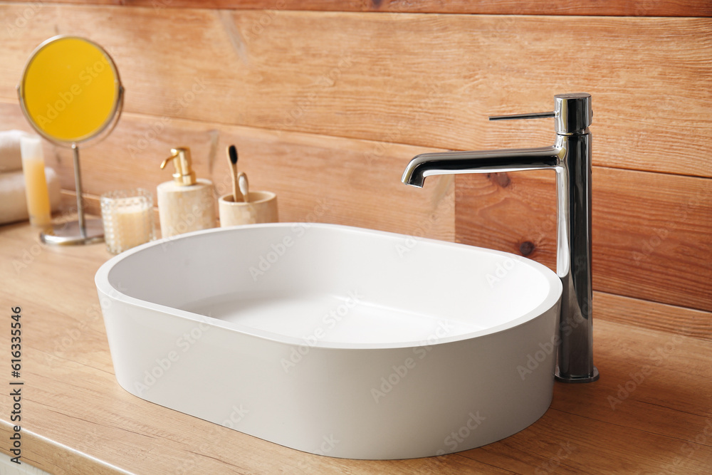 White sink with bath accessories on table near wooden wall