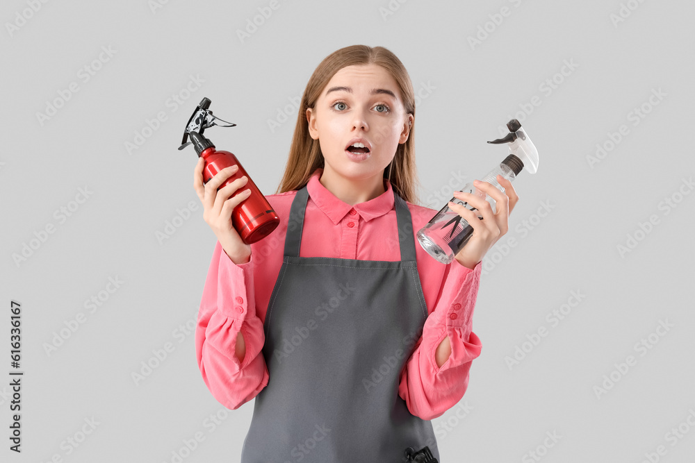 Shocked female hairdresser with sprays on grey background