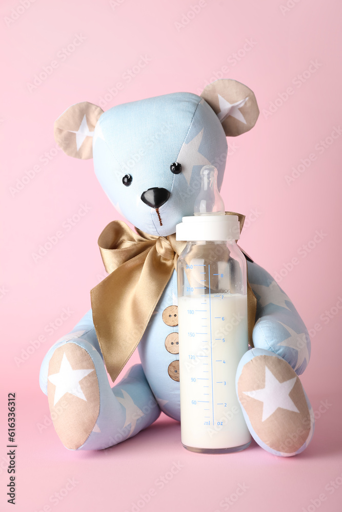 Teddy bear with bottle of milk for baby on pink background