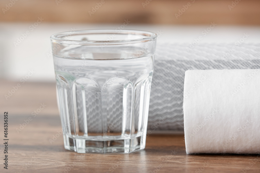 Glass of water with filters on wooden table in kitchen