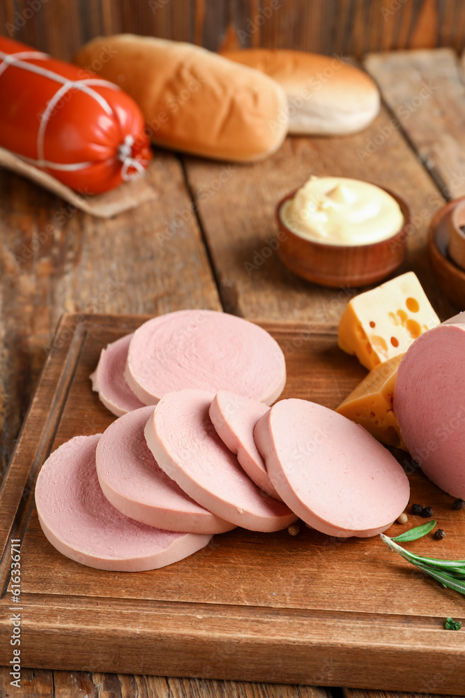 Board with slices of tasty boiled sausage on wooden background