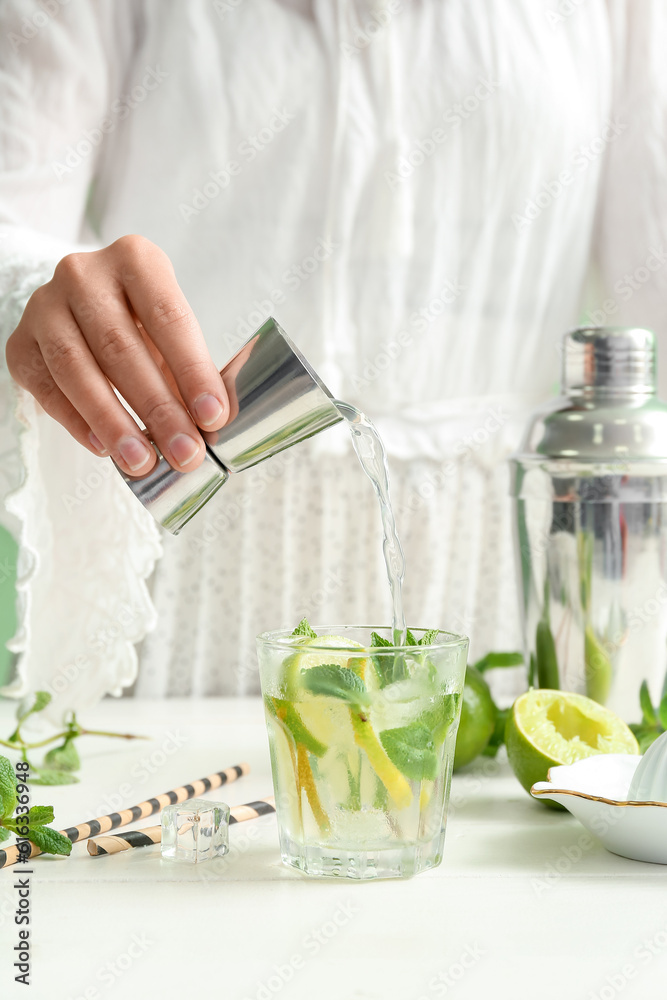 Female bartender making tasty mojito cocktail on white table