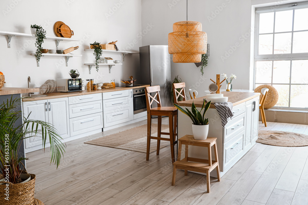 Interior of light kitchen with stylish fridge, counters, shelves and houseplants