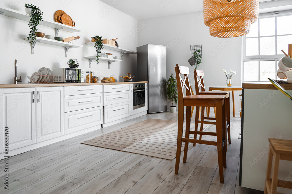 Interior of light kitchen with stylish fridge, counters, shelves and houseplants