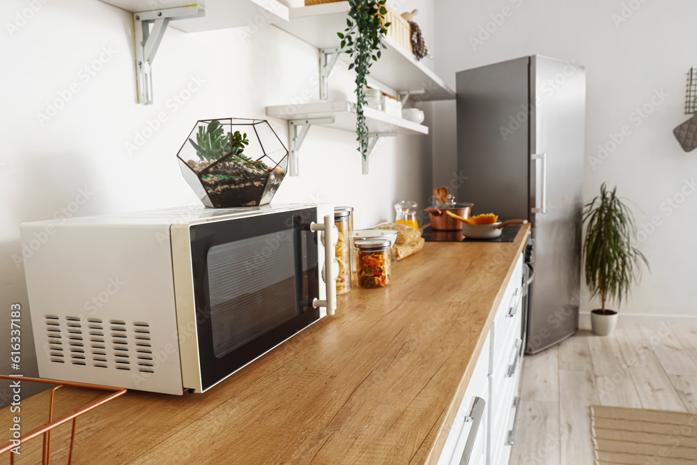 Interior of light kitchen with stylish fridge, counters, shelves and microwave oven, closeup