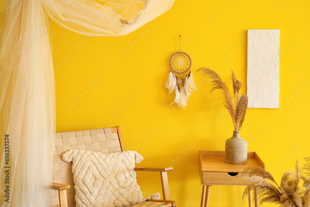 Interior of modern living room with armchair, table and dream catcher hanging on yellow wall