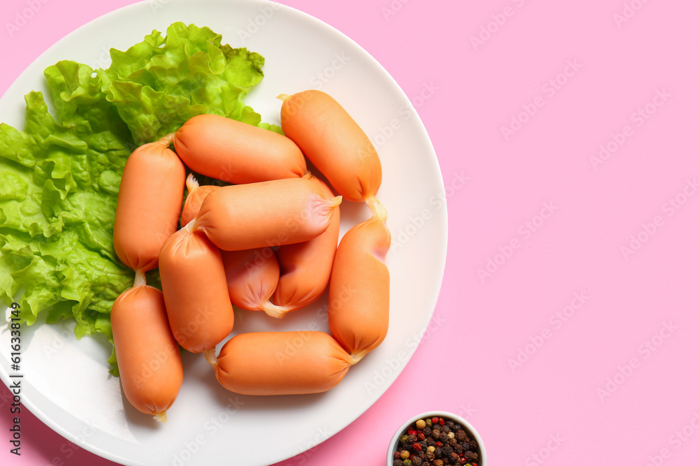 Plate of tasty boiled sausages with lettuce on pink background