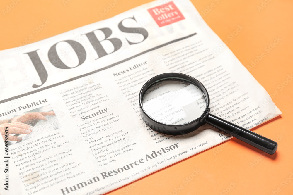 Mini magnifier and newspaper with headline JOBS on orange background. Search concept