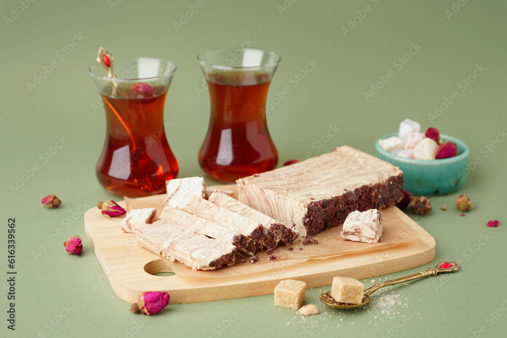 Wooden board with pieces of tasty marble halva on green background