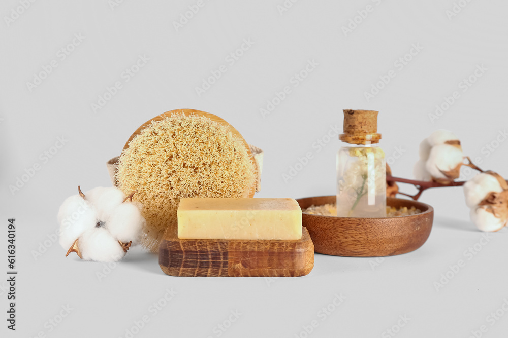 Soap bar, massage brush, sea salt, essential oil and cotton flowers on white background