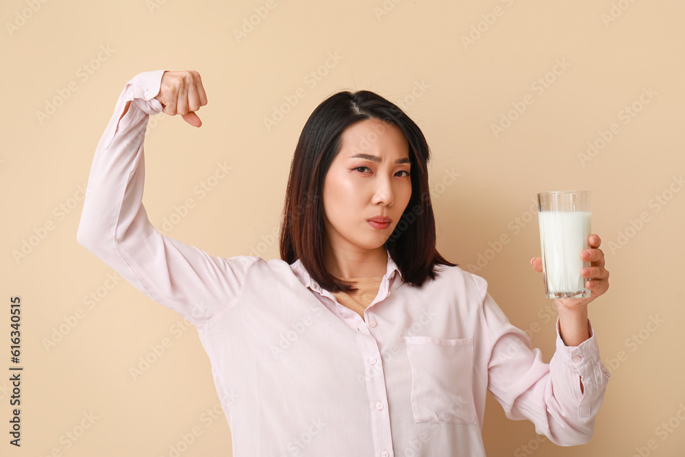 Strong Asian woman with glass of milk on beige background