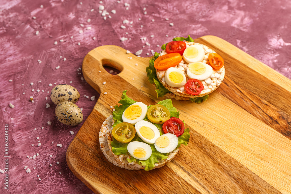 Rice crackers with quail eggs, tomatoes and lettuce on pink background