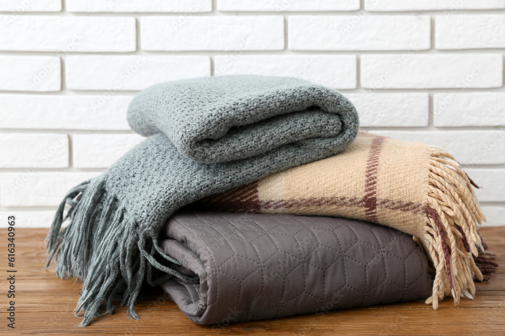 New soft folded blankets on wooden table near light brick wall