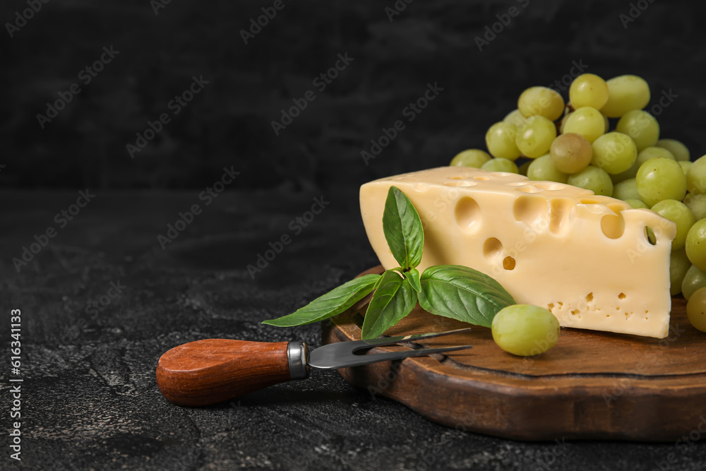 Wooden board with tasty Swiss cheese and grapes on black background