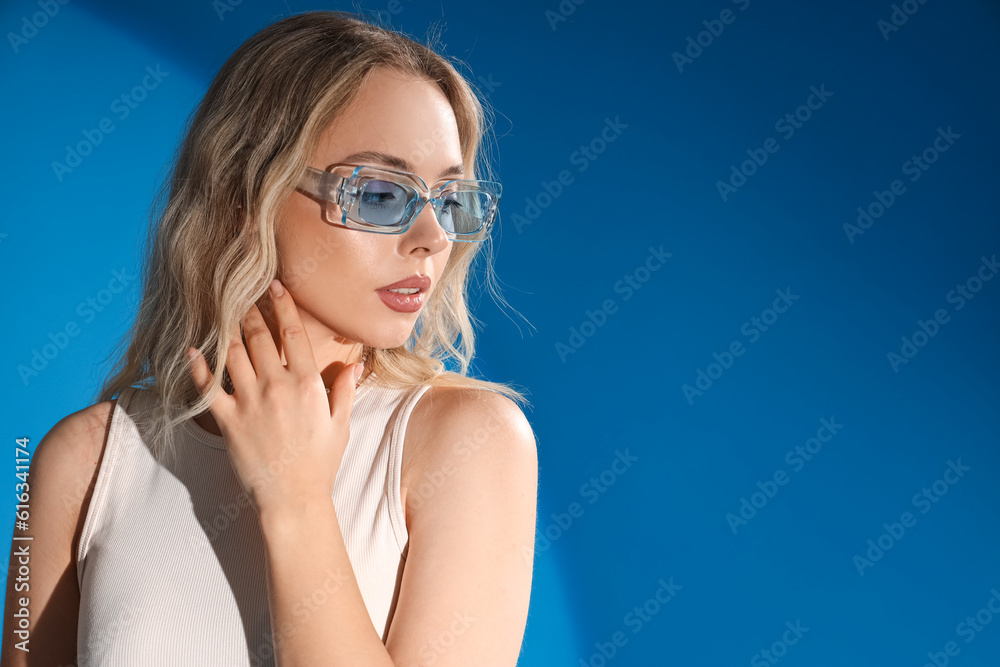 Young woman in stylish sunglasses on blue background, closeup