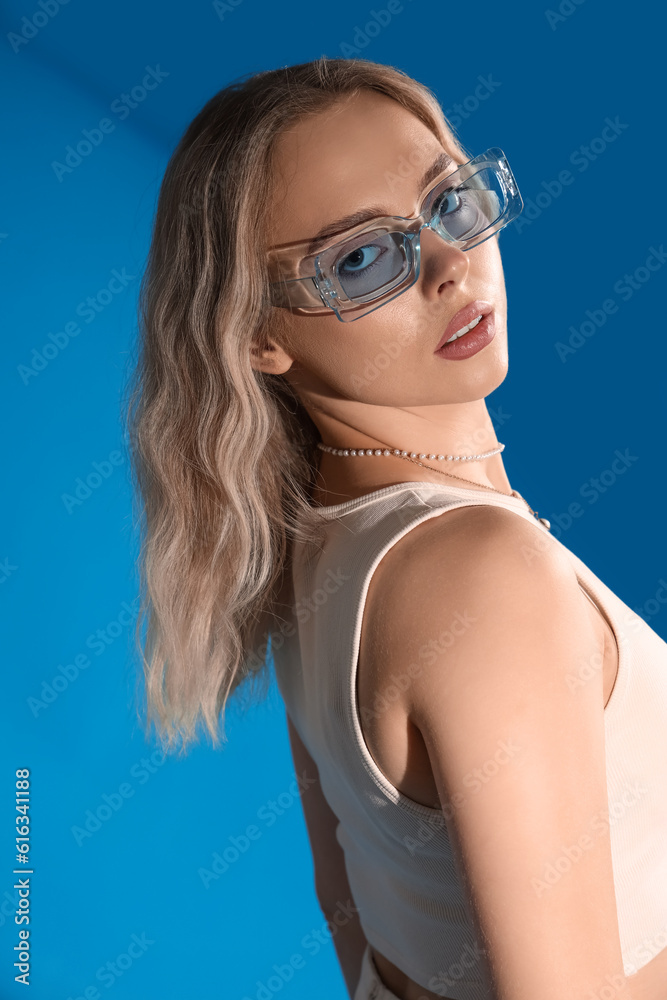 Young woman in stylish sunglasses on blue background, closeup