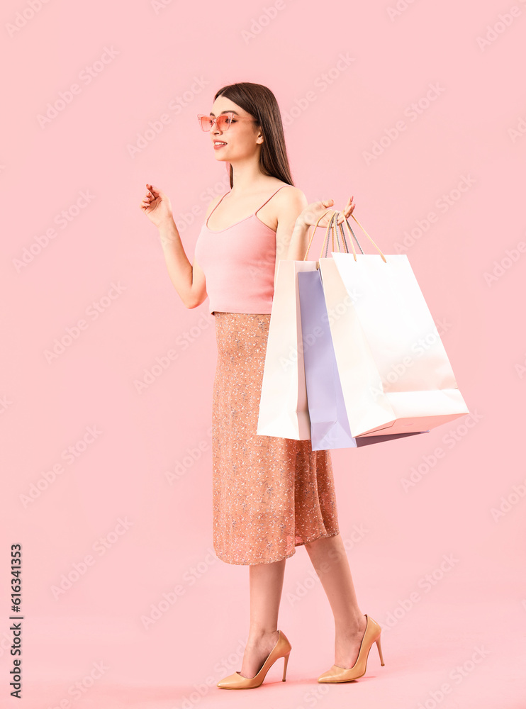 Young woman with shopping bags on pink background