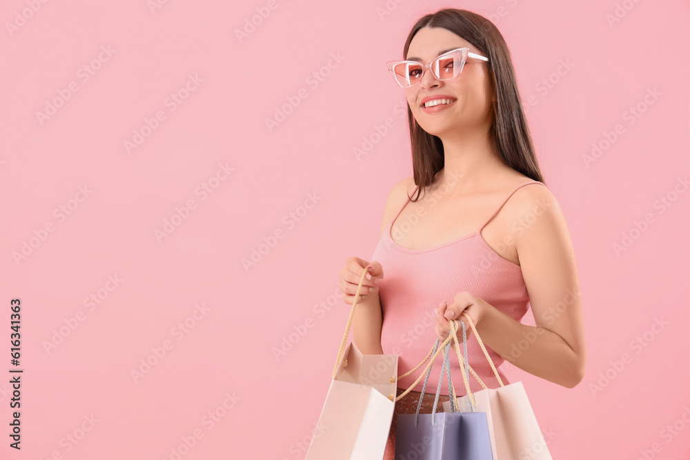 Young woman with shopping bags on pink background