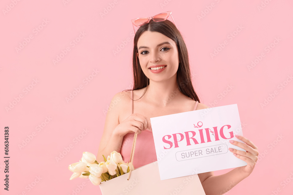 Young woman holding paper with text SPRING SUPER SALE and shopping bag on pink background