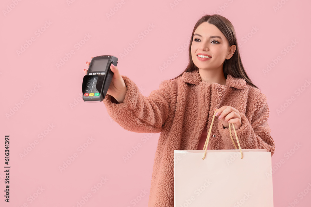 Young woman with shopping bag and payment terminal on pink background