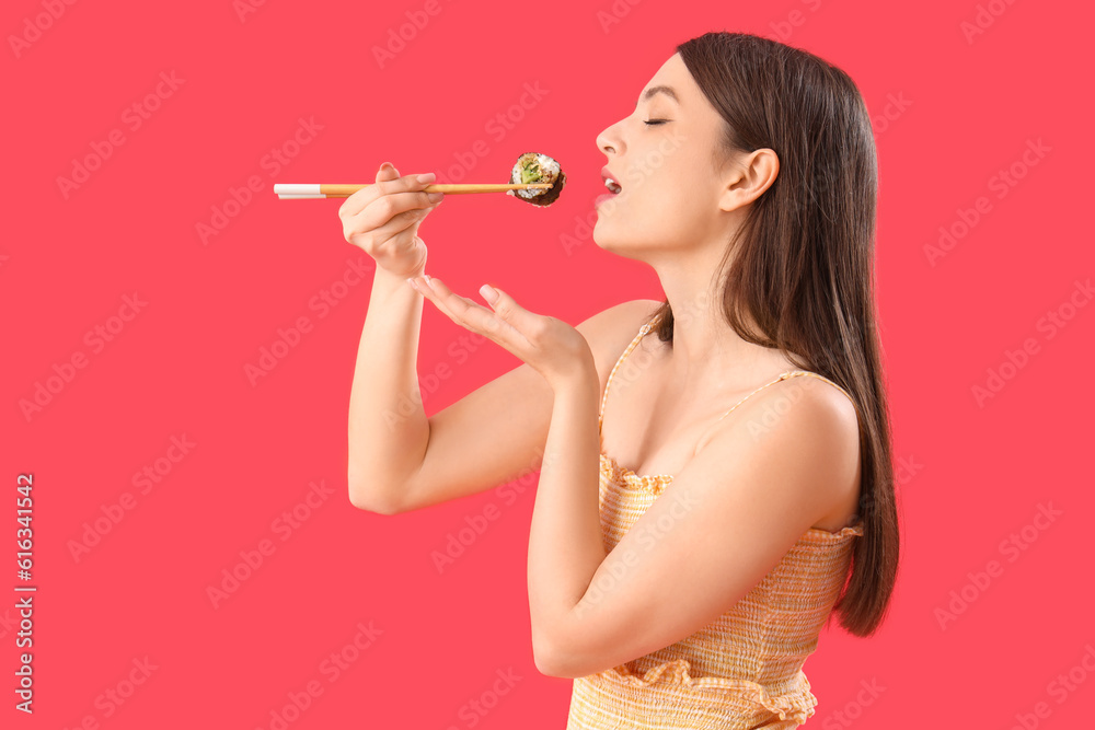 Young woman eating sushi roll on red background