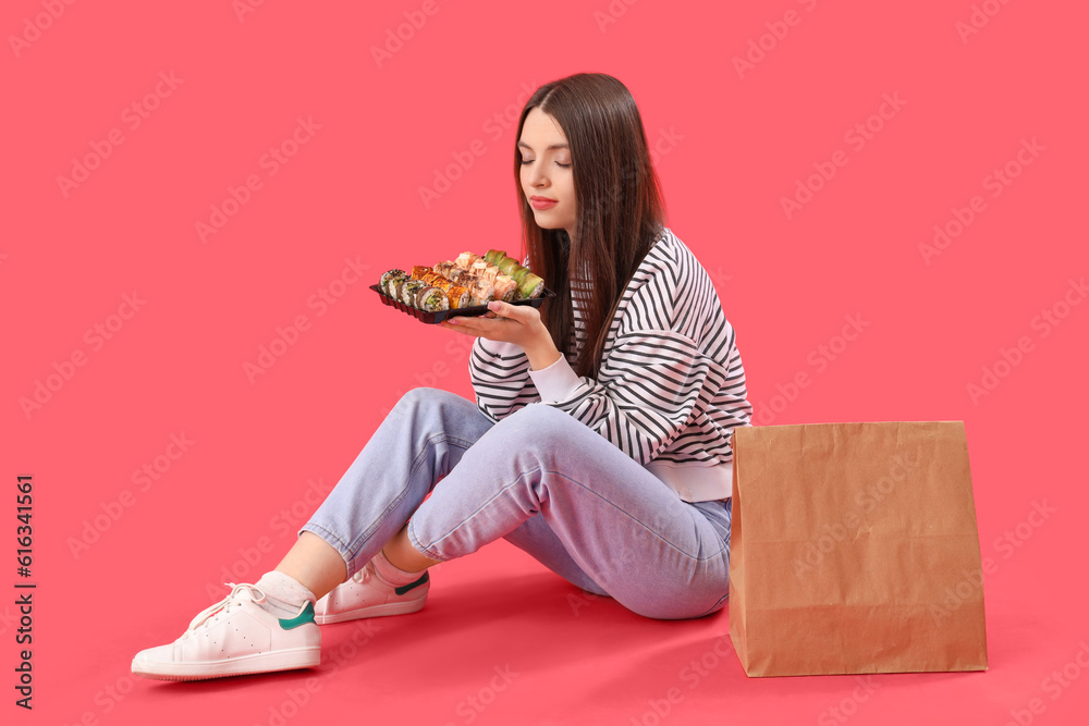 Young woman with sushi and paper bag sitting on red background