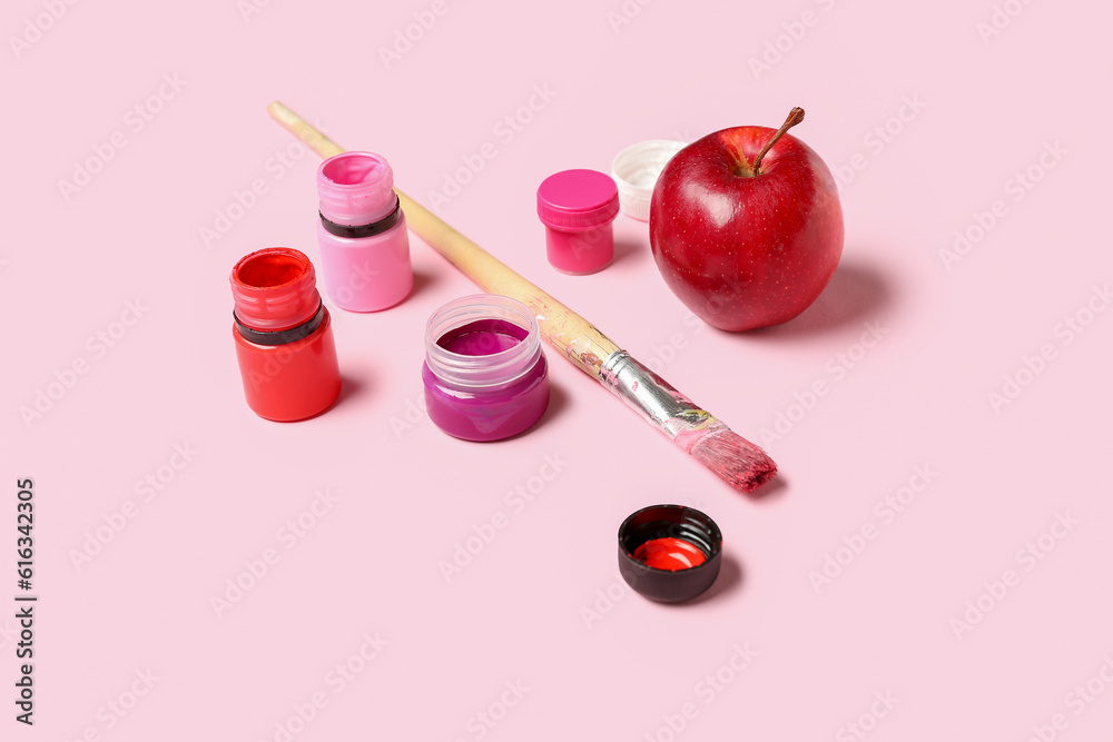 Brush, bottles with different shades of pink paint and apple on color background