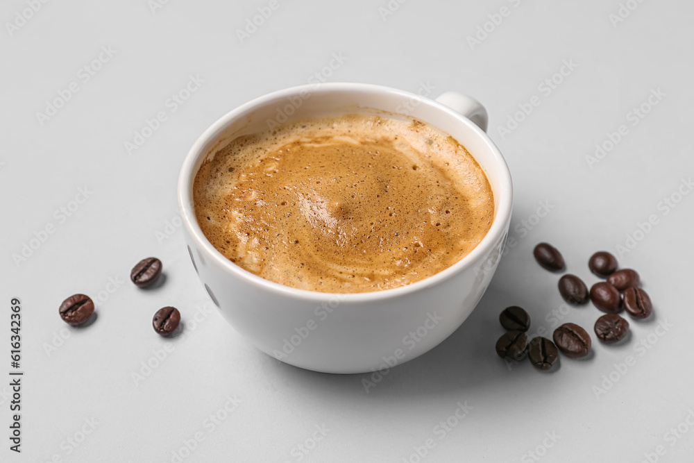 Cup of hot espresso and coffee beans on grey background