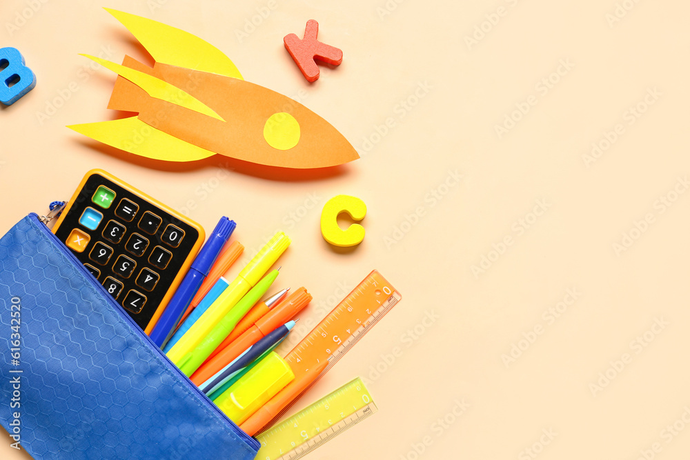 Paper rocket with calculator, pencil case and wooden letters on beige background