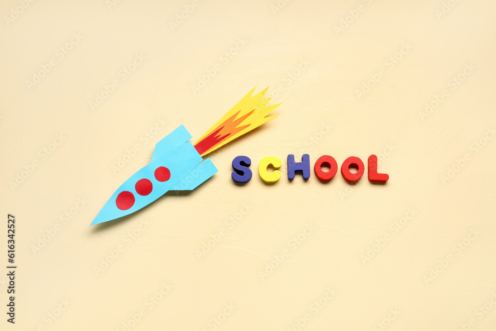 Paper rocket with word SCHOOL on beige background