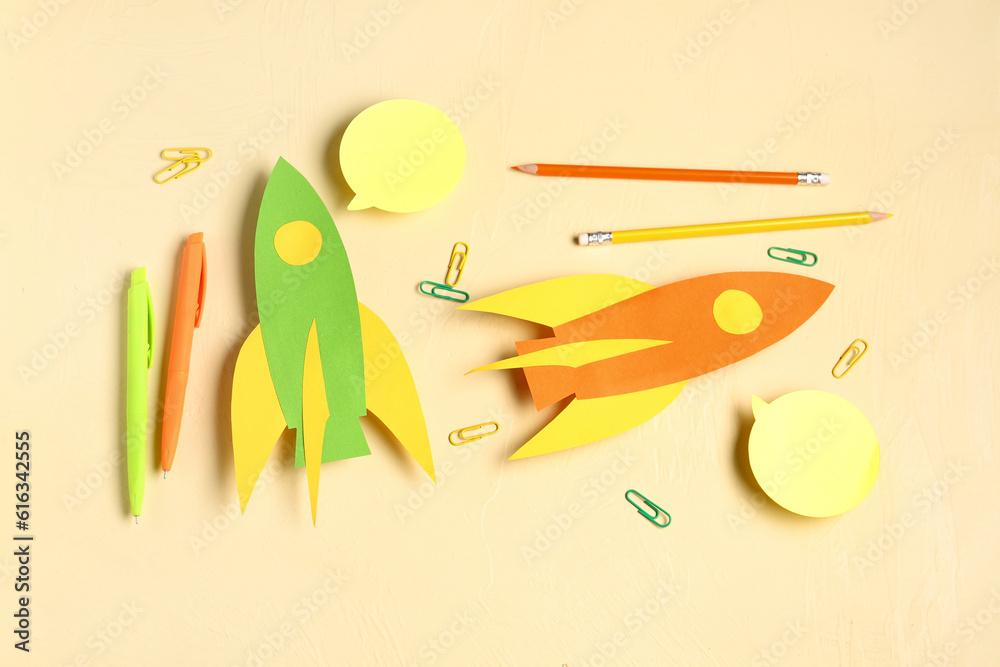 Color paper rockets with pens, pencils and clips on beige background