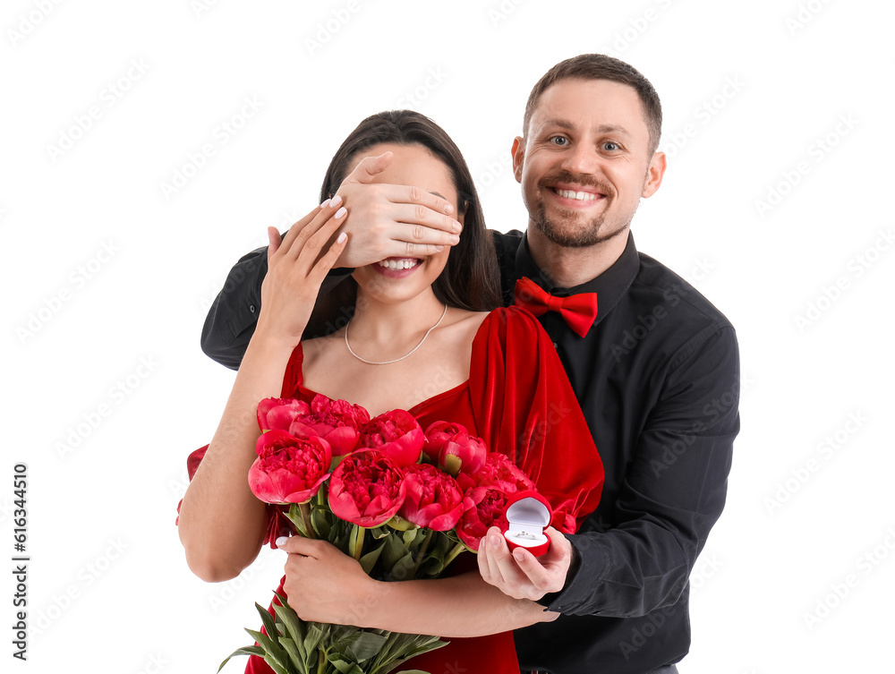 Young man with engagement ring closing his girlfriends eyes on white background